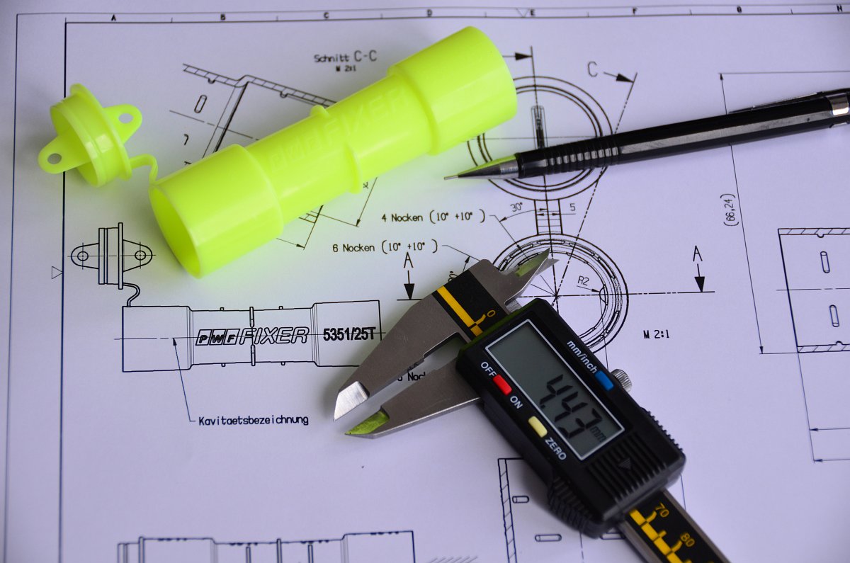 Chi tiết nhựa màu xanh, thước cặp và bút được đặt trên bản vẽ kích thước