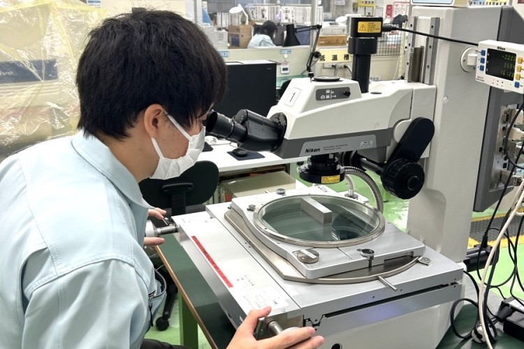 Nhân viên kiểm tra chi tiết nhựa trên bàn kính của thiết bị đo quang học